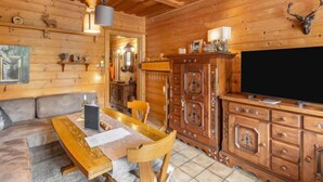 L’intérieur chaleureux d’un chalet en bois comprend une table à manger en bois, un canapé, un meuble avec des tiroirs et un téléviseur fixé au mur.