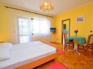 A room with a bed, a television, a table with a vase of flowers, and a chair.