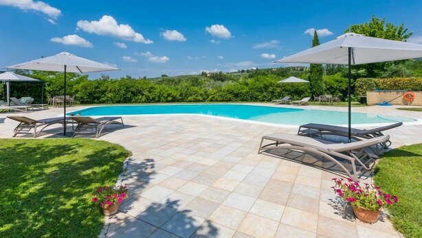 Una piscina con sillas de descanso y sombrillas, rodeada de vegetación y un cielo despejado.