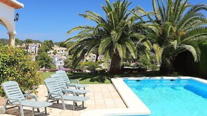 Ein Swimmingpool mit Liegestühlen, Palmen und Häusern im Hintergrund.