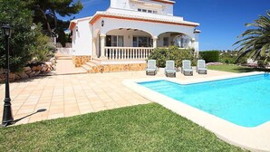 Eine weiße Villa mit Swimmingpool, Sitzgelegenheiten im Freien und einem Kiesweg.