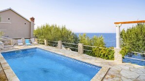 Una piscina con borde de piedra, una pérgola y vista al mar.