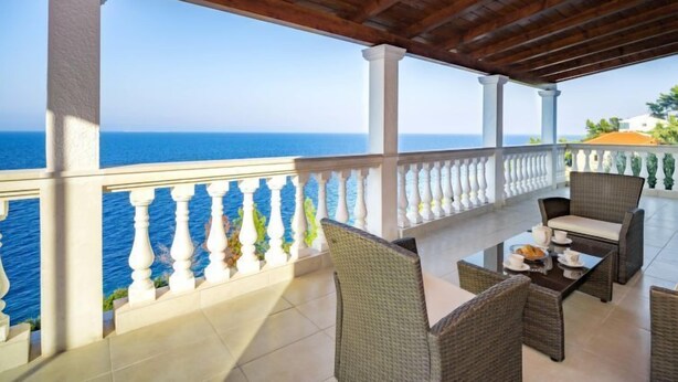 Un espacio de estar al aire libre cubierto con vistas al mar, amueblado con sillas de mimbre y una mesa.