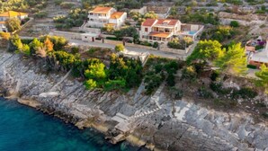 Vista aérea de una zona residencial costera con casas construidas sobre terreno rocoso, con vistas al mar.