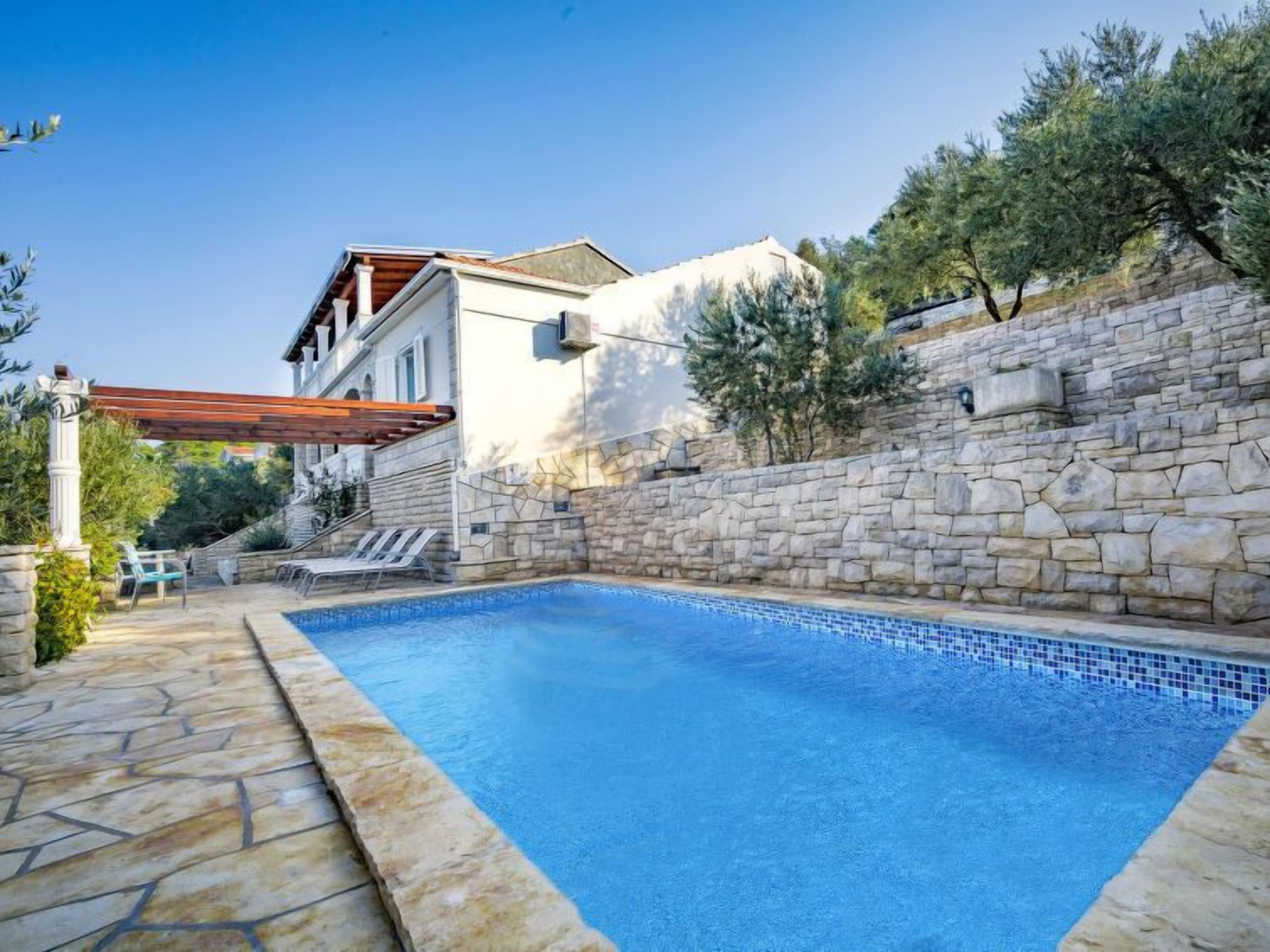 A swimming pool with stone walls and a pergola.