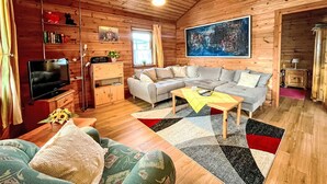 A cozy log cabin interior with a sectional sofa, a flat-screen TV, and a large abstract painting on the wall. - Löwenzahn by Interhome (Adenau)