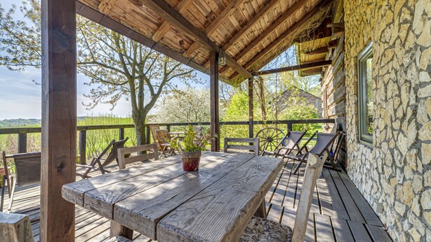A wooden deck with a rustic stone wall, wooden furniture, and a view of the countryside. - Moja Mała Toskania by Interhome (Cisowa)