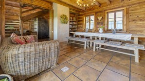 A rustic wooden interior with a wicker sofa, a long dining table, and a chandelier. - Moja Mała Toskania by Interhome (Cisowa)