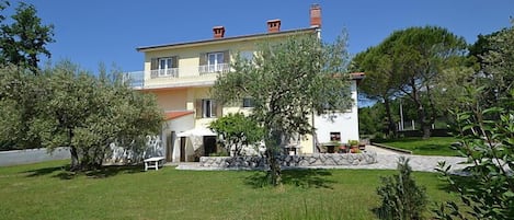 A two-story house with a balcony, surrounded by a well-maintained lawn and trees.