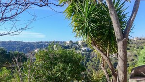 A garden with a stone sculpture, a palm tree, and a view of a hilly landscape with buildings in the distance. - Vacation home Agora by Interhome (Nice)