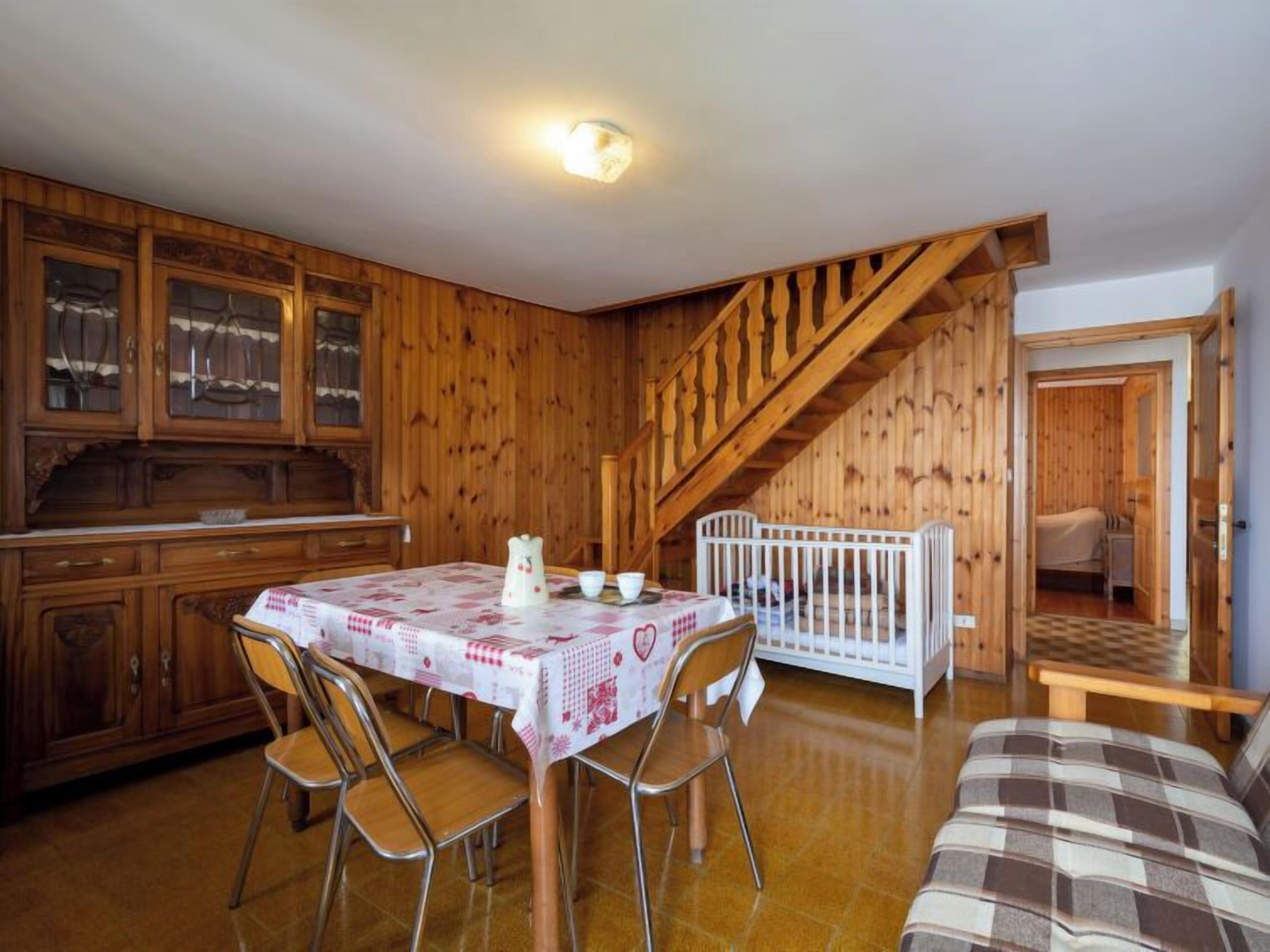 A wooden interior with a dining table, chairs, a crib, and a staircase.