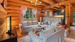Interno di una baita in legno con un angolo soggiorno accogliente, caratterizzato da divani a righe, una parete decorata in pietra, travi in legno e una zona cucina.