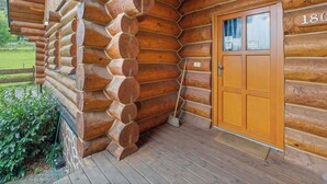 Una baita di legno con una porta in legno con il numero '180' e un portico con una scopa appoggiata al muro.