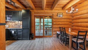 Interno di una baita di legno con cucina, zona pranzo e vista sull'esterno.