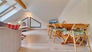 A cozy attic room with a wooden dining table and chairs, a sofa, and a TV. - Kubaczka by Interhome (Wisla)