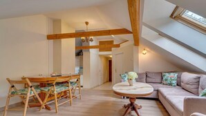 A spacious living area with a high ceiling, wooden beams, a round table with a vase, a sofa with cushions, and a view through a skylight. - Kubaczka by Interhome (Wisla)