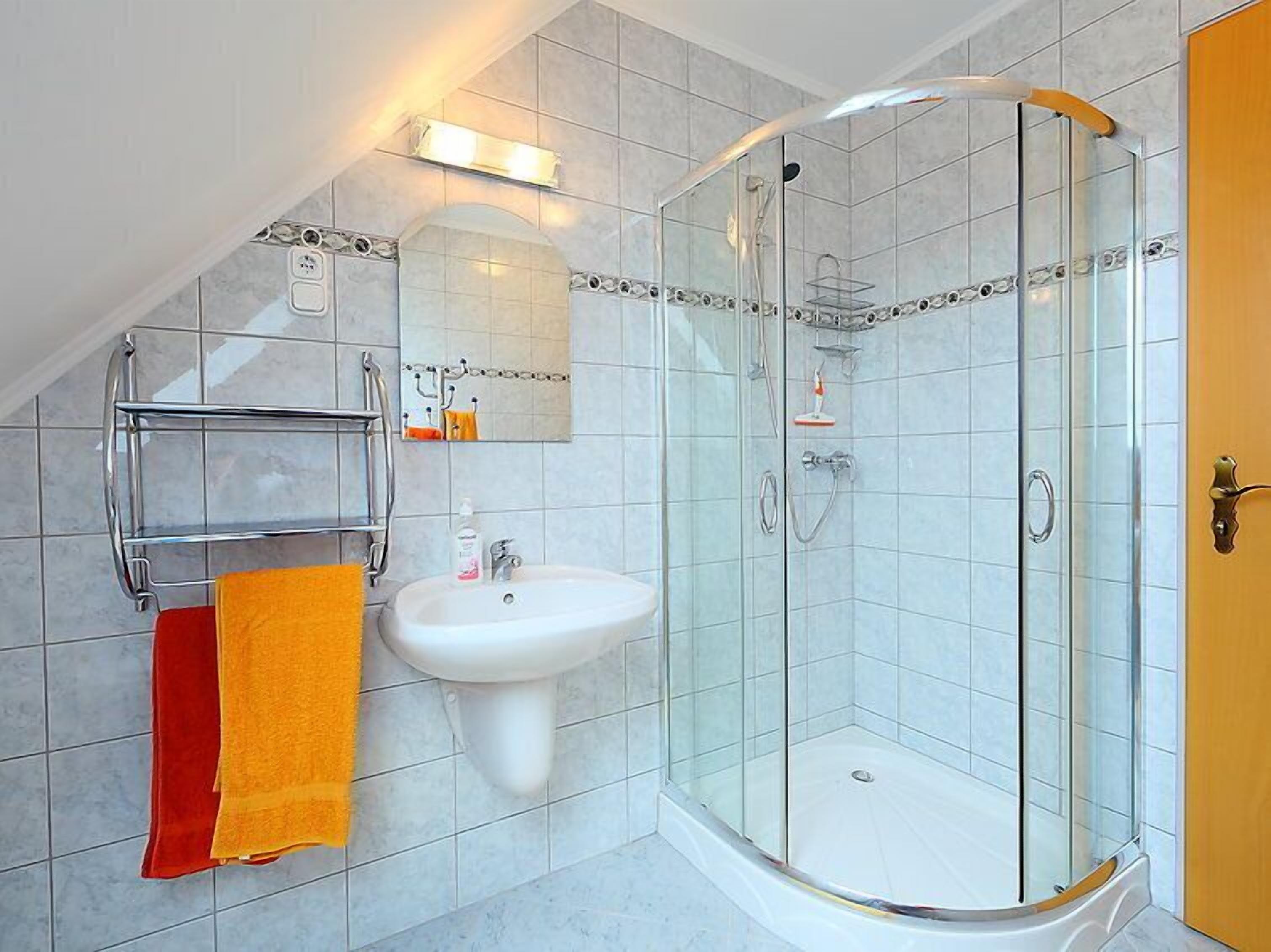 Une salle de bain moderne avec une douche à parois de verre, un lavabo blanc et un porte-serviettes avec des serviettes rouges et jaunes.
