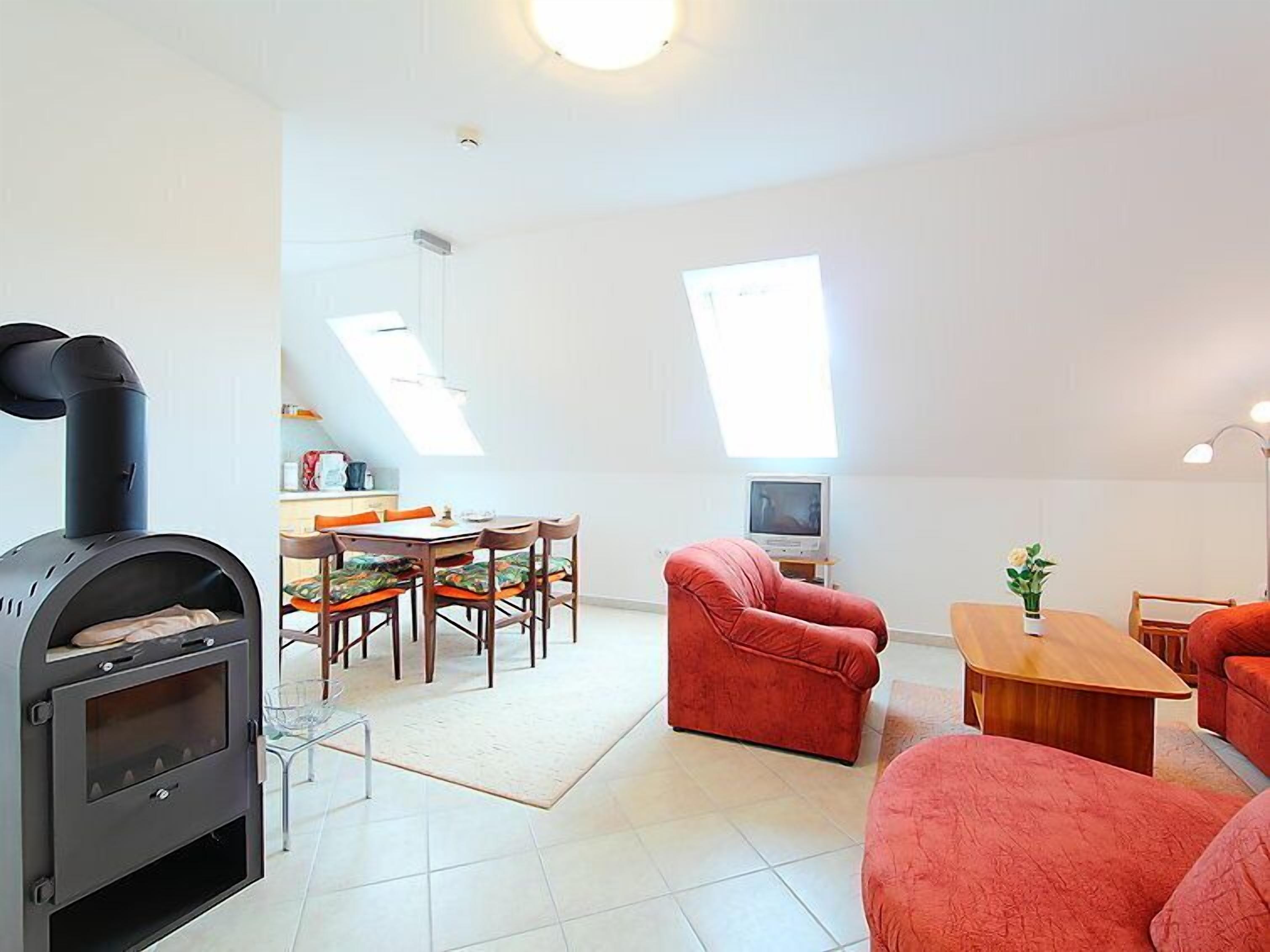 En moderne stue med pejs, røde sofaer, et spiseområde og ovenlysvinduer.