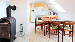 A modern kitchen with a black wood stove, wooden cabinets, and a dining area with a table and chairs.