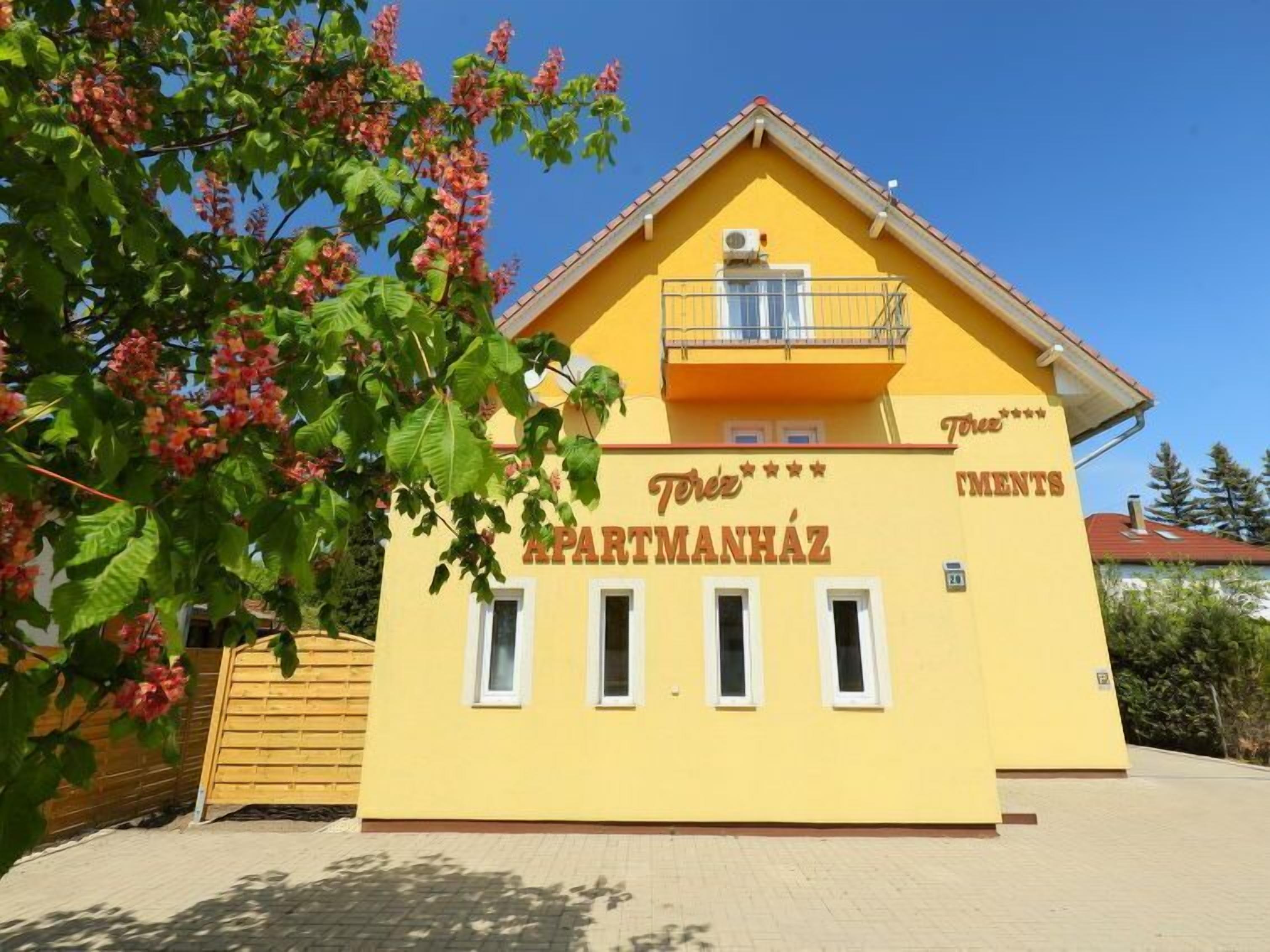 Un immeuble jaune avec une enseigne indiquant « Terez Apartmanhaz » et un balcon.
