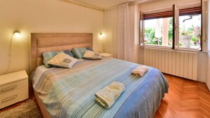 Une chambre à coucher comprenant un lit, des tables de chevet, une fenêtre avec des rideaux et un luminaire au plafond.