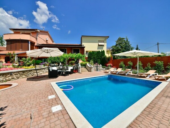 A rectangular swimming pool with a brick border, surrounded by lounge chairs and umbrellas.