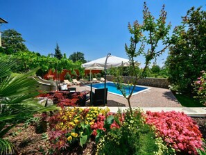 A swimming pool with lounge chairs and umbrellas, surrounded by a garden with various plants and flowers. - Apartment Lidija by Interhome (Opatija/Matulji)
