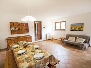 A dining area with a table set for four, a wooden cabinet, a sofa, and a radiator.