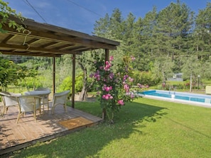 A covered patio with outdoor furniture, a swimming pool, and a garden with flowering plants.