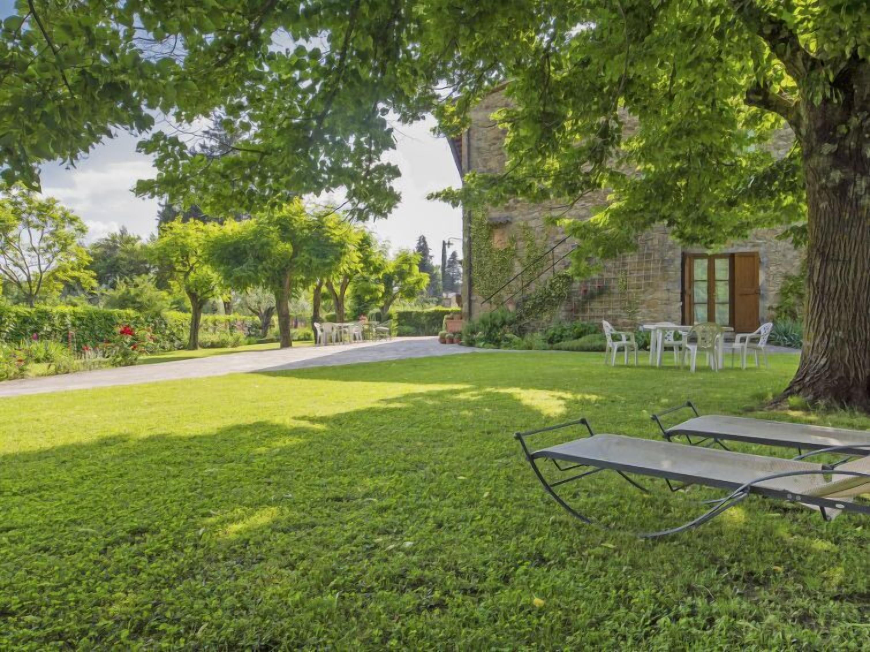 A grassy outdoor area with a stone building, a pathway, and outdoor seating.