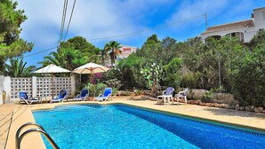Piscina com espreguiçadeiras e guarda-sóis, cercada por vegetação e uma cerca branca.
