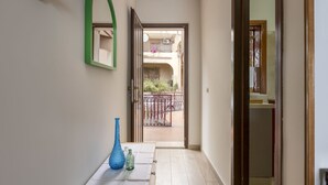Un couloir avec un plancher en bois, une table blanche sur laquelle reposent deux bouteilles en verre, un objet en forme de cœur de couleur verte et un miroir avec un cadre vert.