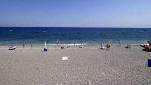 Une plage avec un ciel dégagé, une mer calme, ainsi que plusieurs parasols et chaises de plage.