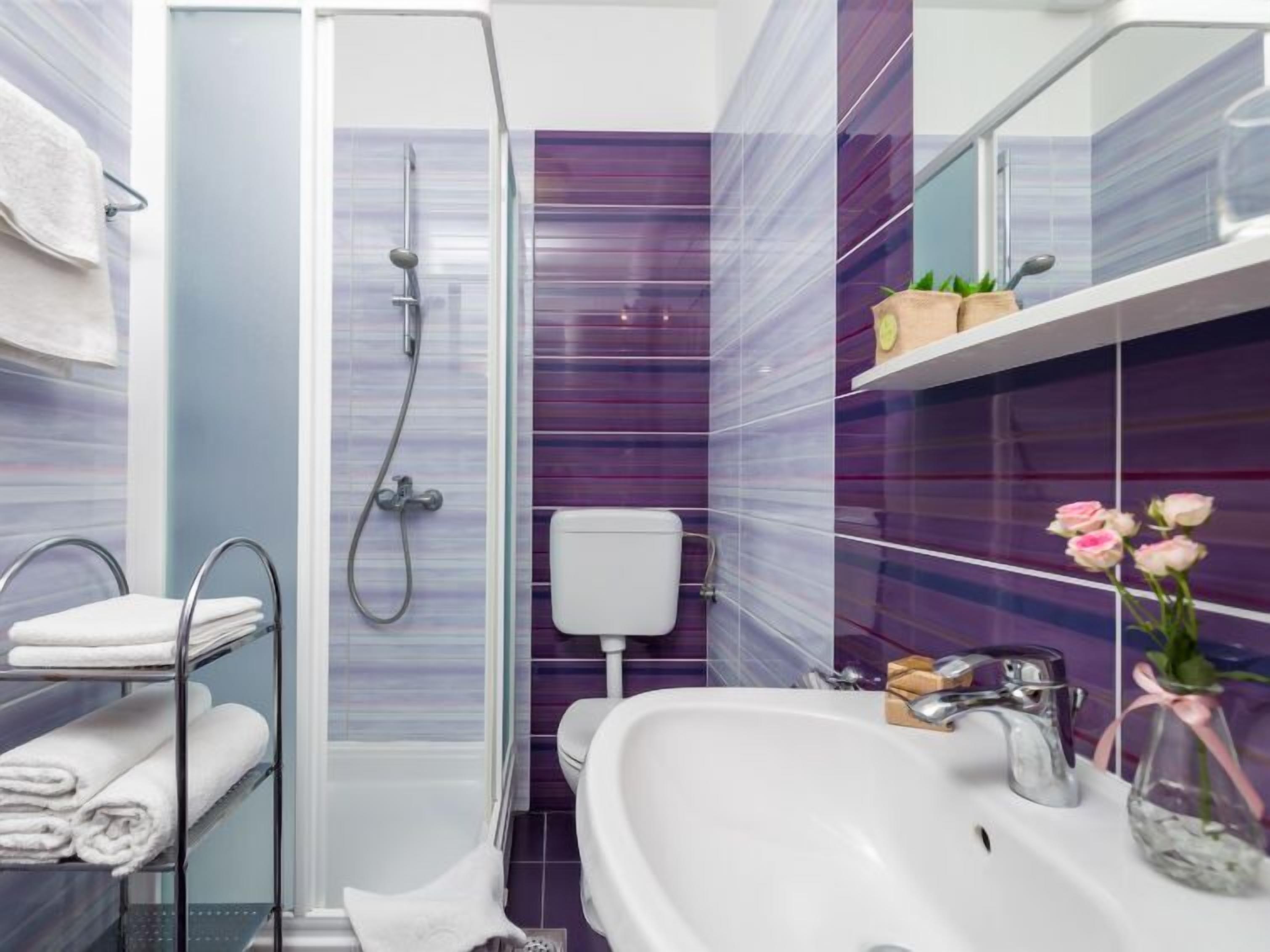 Une salle de bain moderne avec une douche à parois de verre, un lavabo blanc et des murs recouverts de carreaux violets.