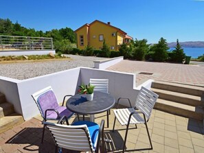 Un patio al aire libre con una mesa redonda y cuatro sillas, una planta en maceta y un edificio amarillo al fondo.
