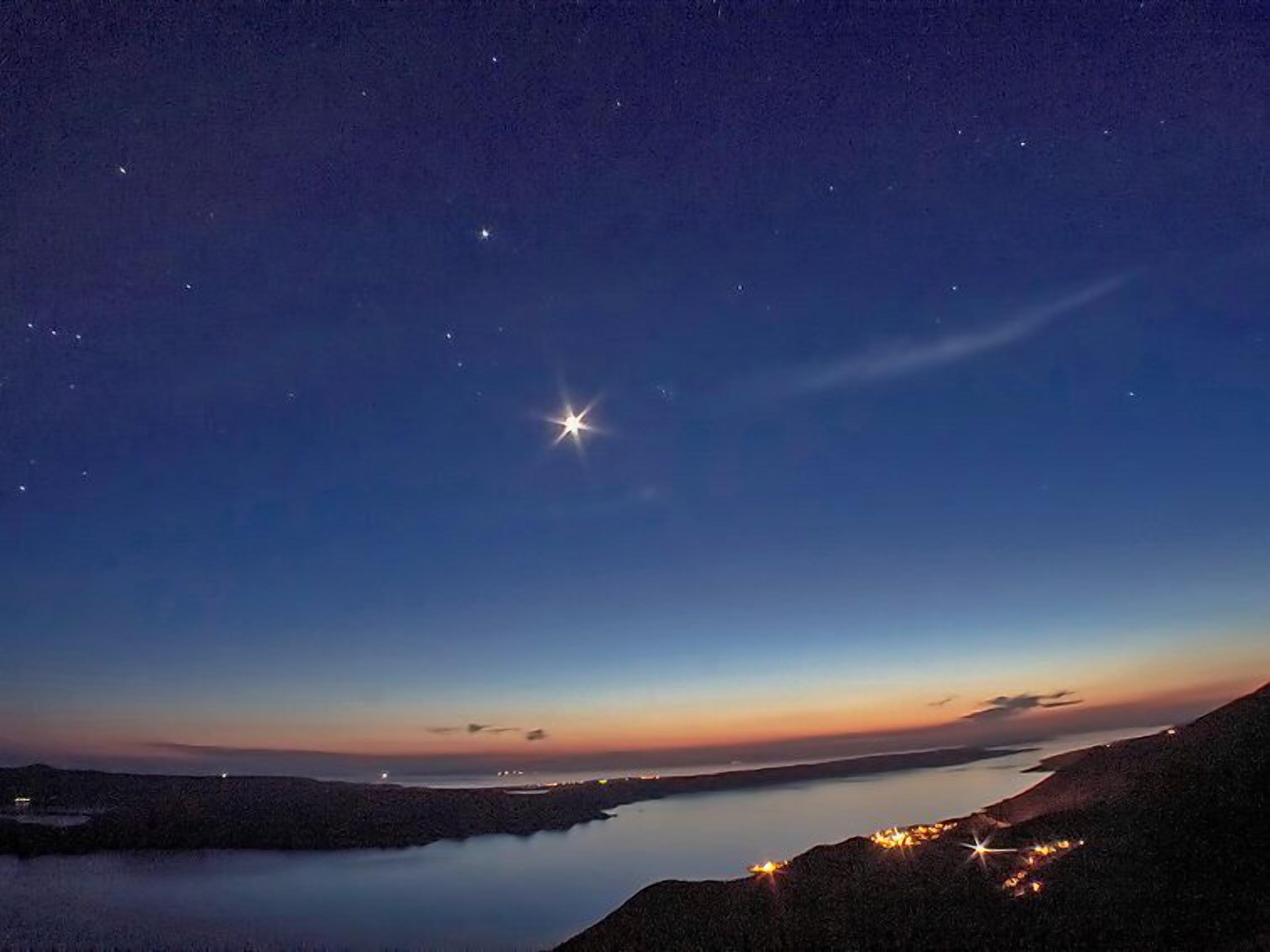 A night sky with stars and a bright star near the horizon.