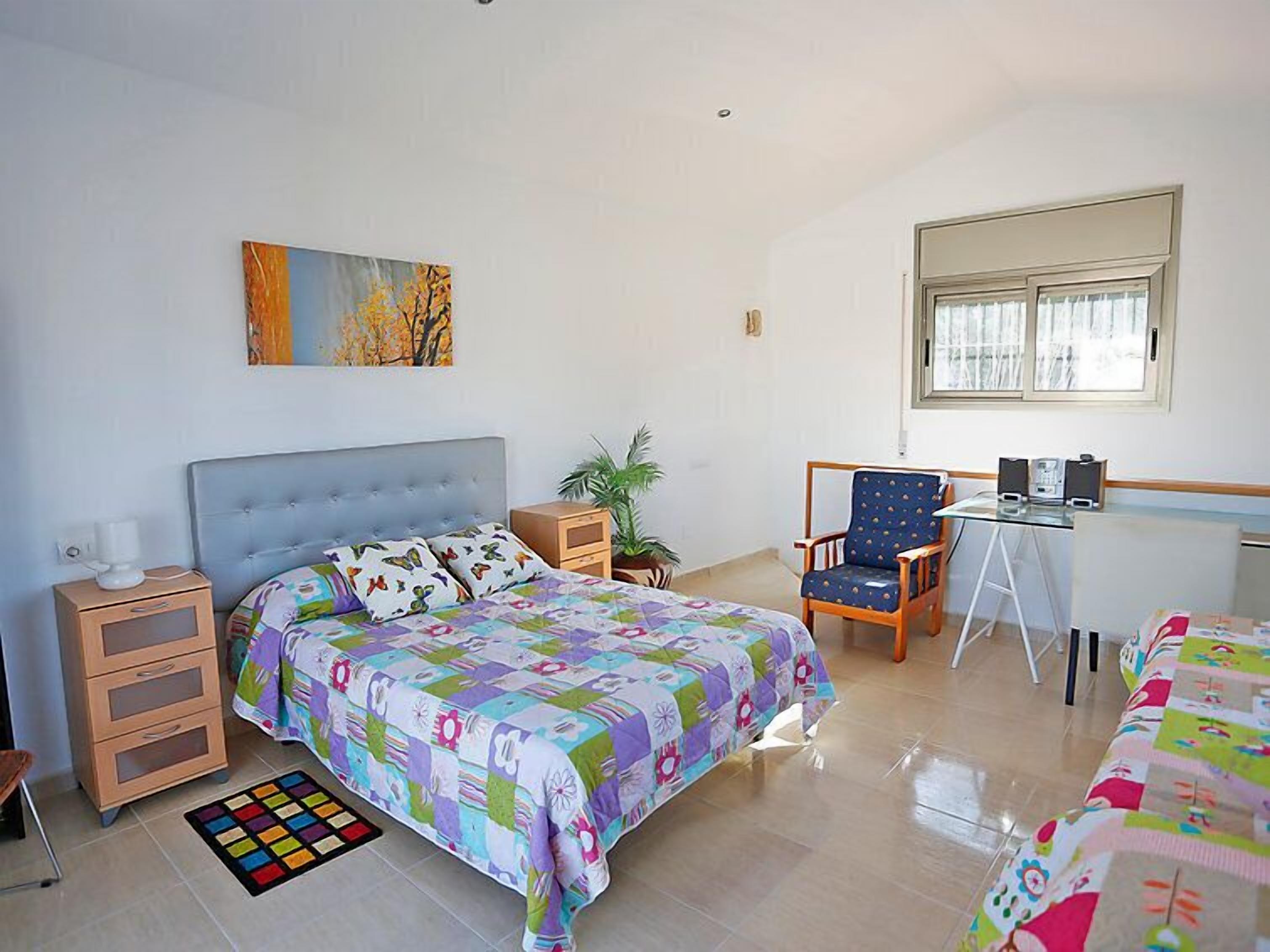 Un dormitorio con una cama, un escritorio, una silla, una planta y un cuadro en la pared.