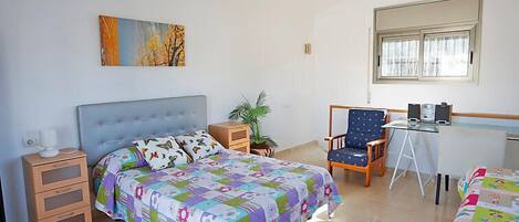 Un dormitorio con una cama, un escritorio, una silla, una planta y un cuadro en la pared.