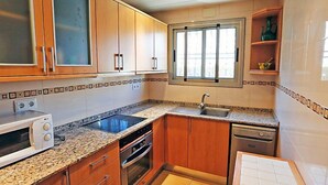 A compact kitchen with wooden cabinets, a built-in microwave, a stove, a sink, and a dishwasher.
