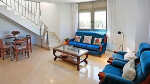 A spacious living room with a blue sofa, a glass coffee table, and a dining area with wooden chairs and a table.