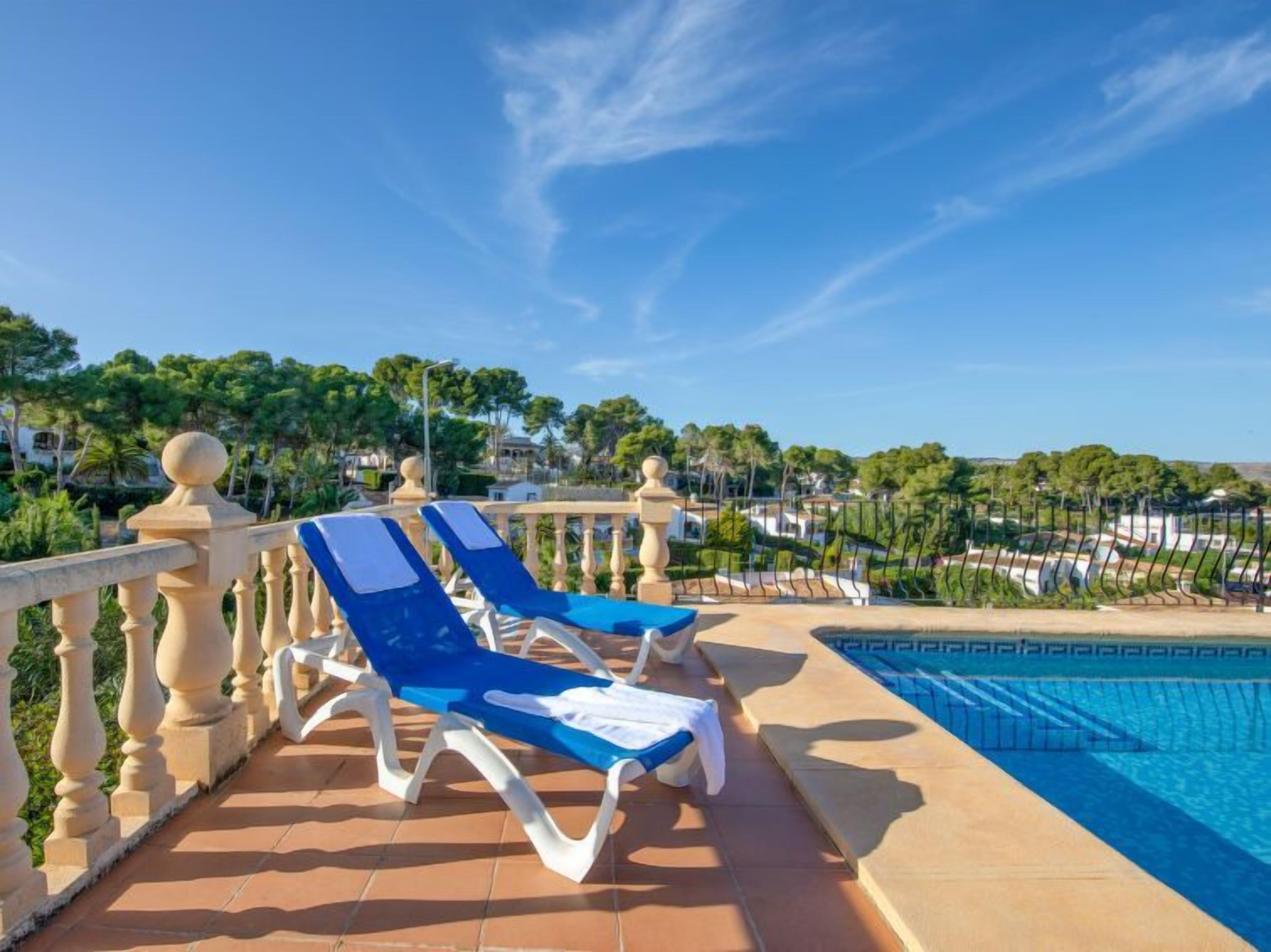 A poolside area with two blue lounge chairs and a tiled floor.