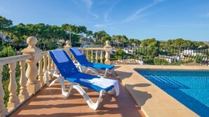Un área junto a la piscina con dos sillones reclinables azules y suelo de baldosas.