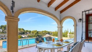 Terraza con vista a una piscina, mesa y sillas blancas, y cielo despejado.