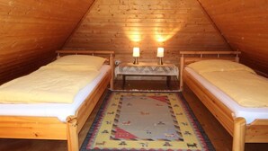 Un dormitorio pequeño de madera estilo altillo con dos camas individuales, un banco y una alfombra estampada.