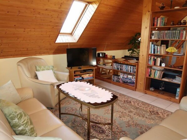 Un salon chaleureux avec un plafond haut, une télévision, une bibliothèque et un canapé confortable.
