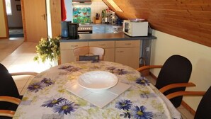 Una cocina acogedora con paredes de madera, un rincón de comedor con mantel floreado y vista al salón.
