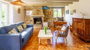 Una sala de estar con chimenea de piedra, sofá azul, mesa de centro de madera y televisor sobre un mueble de madera.
