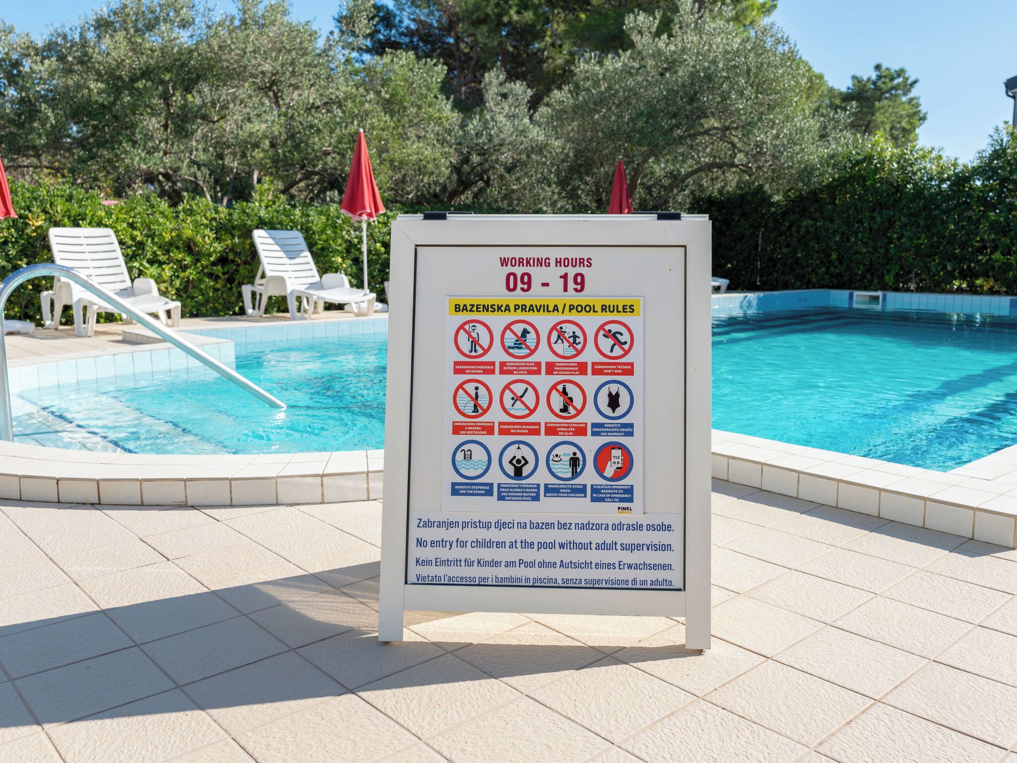 A poolside sign with pool rules and working hours.