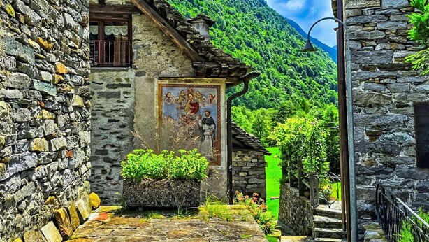 Un edificio de piedra con fachada rústica, un pequeño balcón y un mural en la pared.
