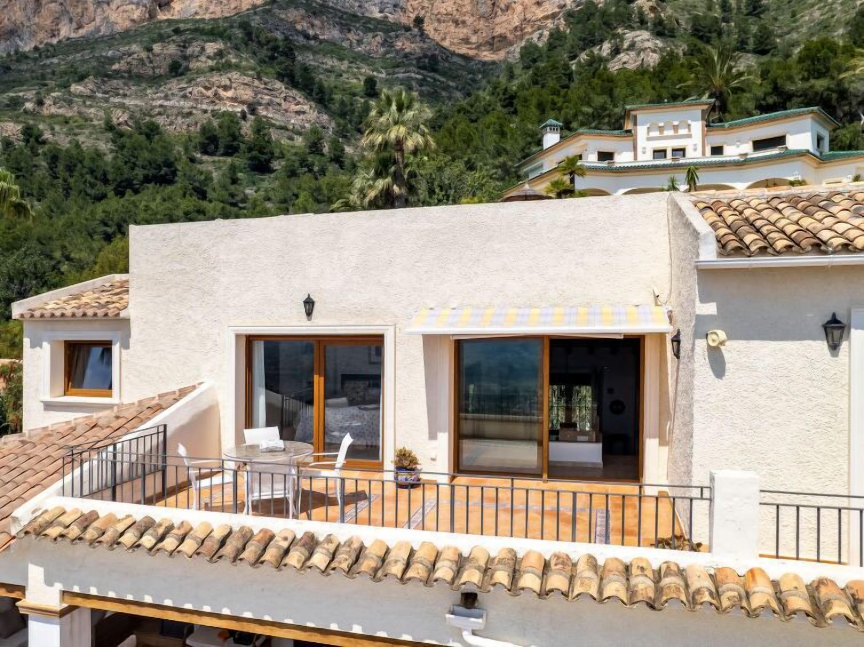 Een villa in mediterrane stijl met balkon, grote ramen en uitzicht op de omliggende heuvels.